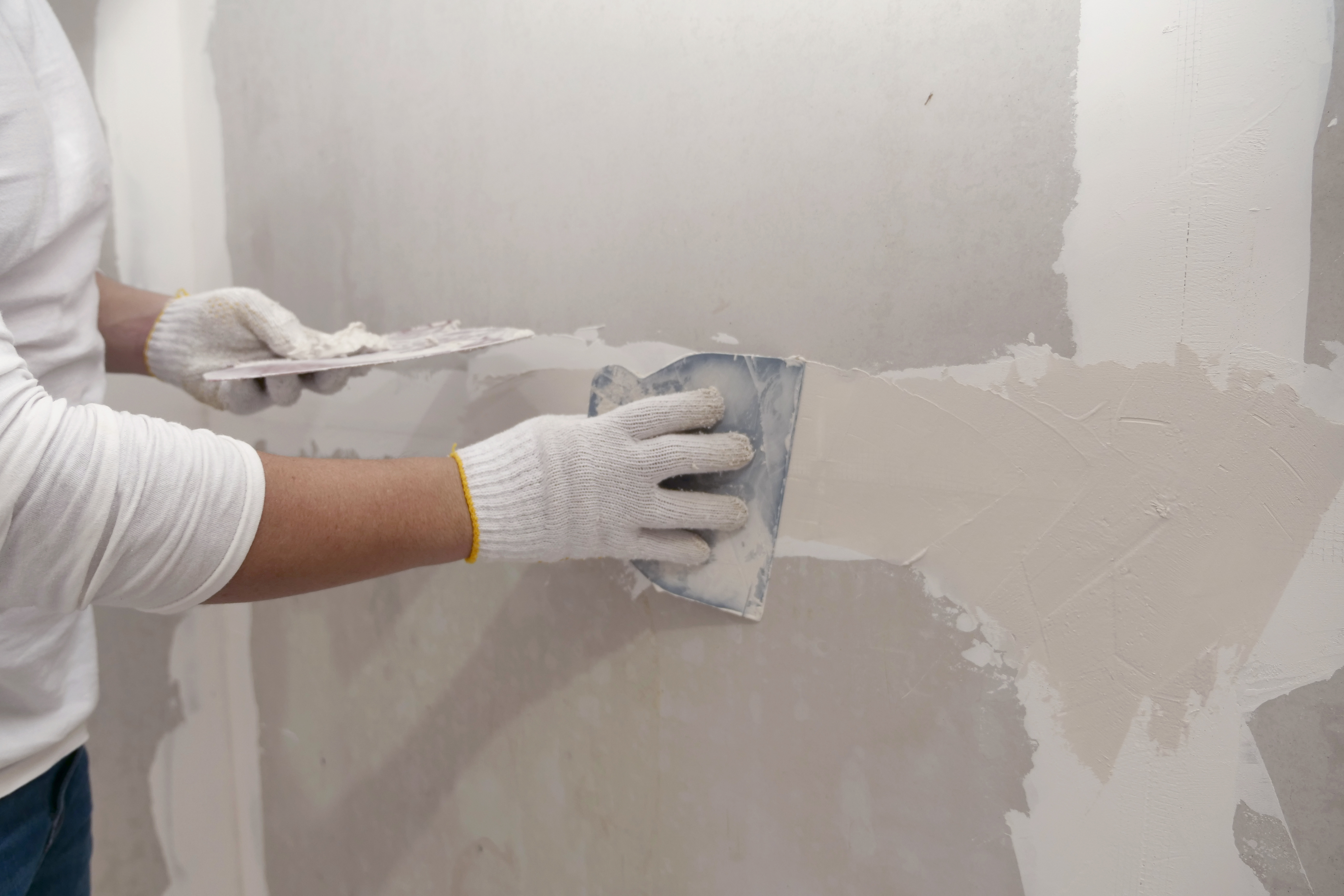 Worker in white gloves applying joint compound to drywall with putty knife