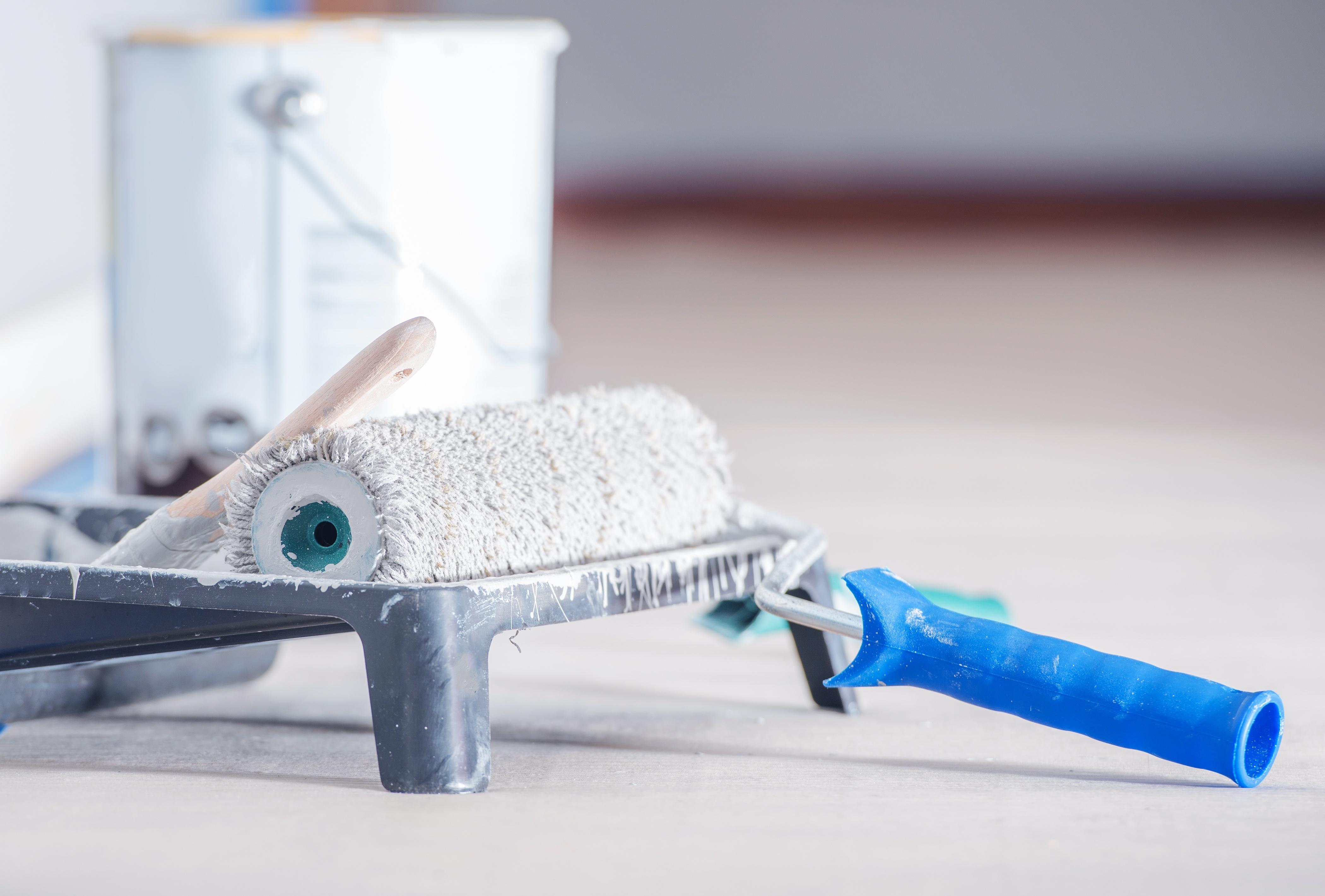 Paint roller with white paint coating and blue handle on surface with paint can