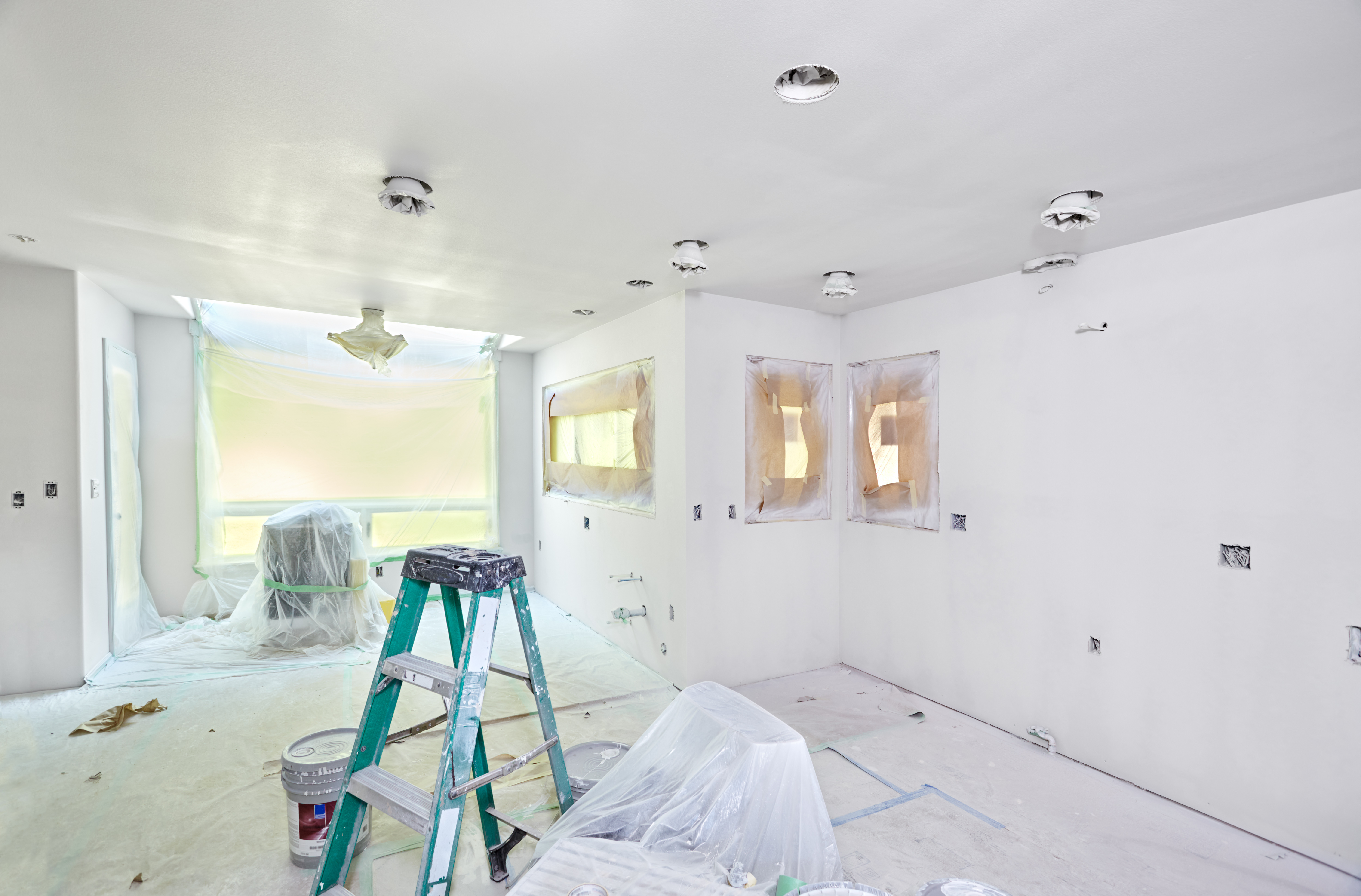 Interior room under construction with drywall, ladder, protective coverings, and recessed ceiling lights